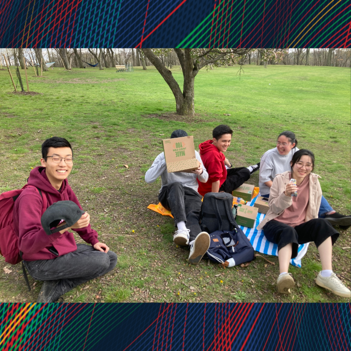 A group of people, sitting in the grass, smile while others look on