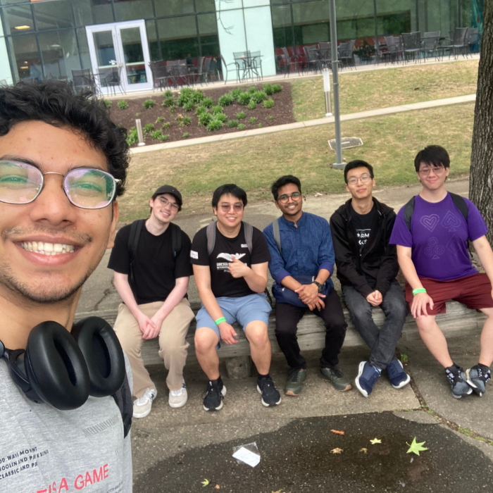 A man in the foreground of the photo takes a selfie with a group sitting to his left