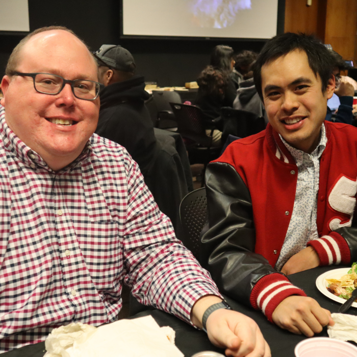 Two men sit at a table, smiling at the camera