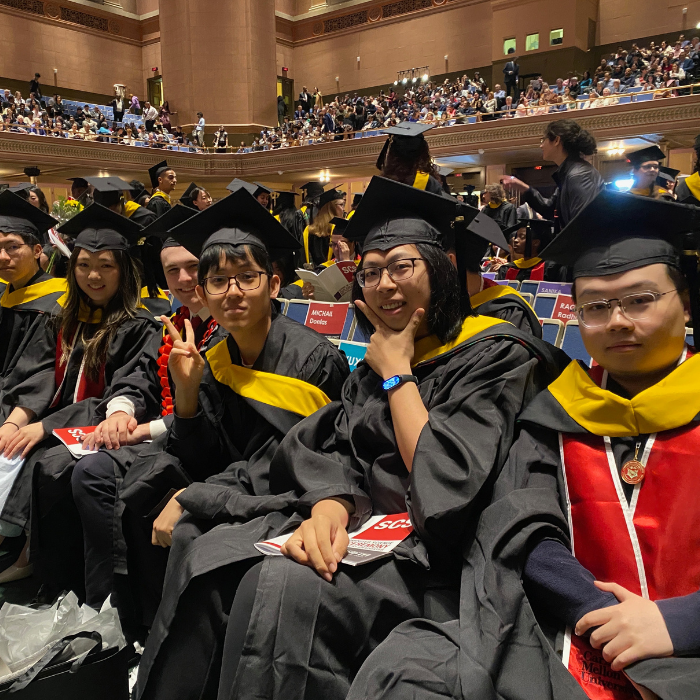A group sits in a line wearing academic regalia and poses for the camera