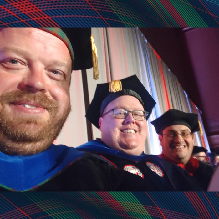 Three men pose for a selfie wearing graduation regalia