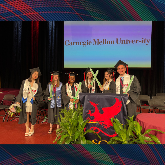 A group of students stand together posing wearing academic regalia holding pixelated swords